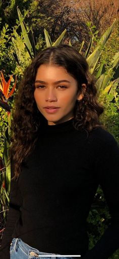 a young woman standing in front of some plants and flowers with her hands on her hips