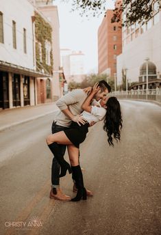 two women are hugging on the street in front of some buildings and one woman is wearing boots