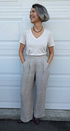 an older woman standing in front of a garage door wearing wide legged pants and a white t - shirt