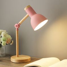 a pink lamp sitting on top of a wooden table next to a vase with flowers