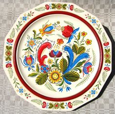 a decorative plate with flowers and birds painted on the side, sitting on a table cloth