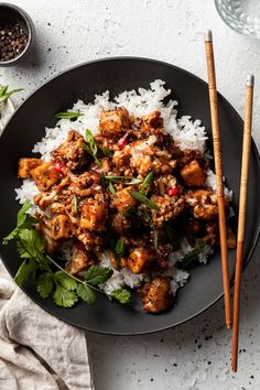 a black plate topped with chicken and rice next to chopsticks on a table