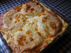 a square casserole dish with cheese and sauce on the top is sitting on a checkered tablecloth