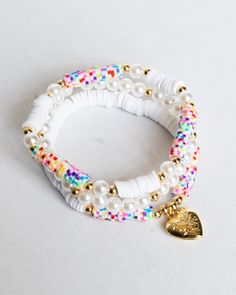 two bracelets with white beads and gold heart charms on each one, both decorated with multi - colored seed beads