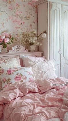 a bed with pink comforters and pillows in a room that has floral wallpaper on the walls