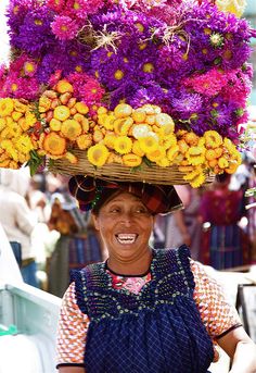 a woman wearing a basket full of flowers on top of her head and smiling at the camera