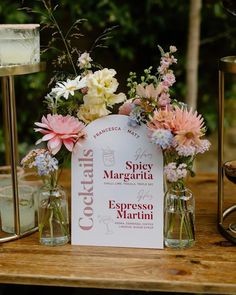 a table topped with vases filled with flowers next to a sign that says spicy margarita espresso martini