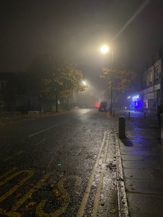 an empty street at night with lights on and cars parked in the road behind it