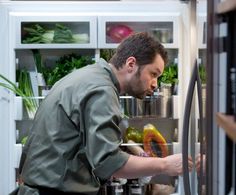 a man is looking in the refrigerator for something to eat and he's trying to get some fresh produce