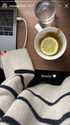 a cup of tea next to a laptop on a table with a lemon slice in it