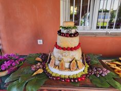 a three tiered cake with fruits and vegetables on it sitting on a table in front of a window