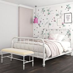 a white bed sitting in a bedroom next to a pink lamp and wallpaper with flowers on it