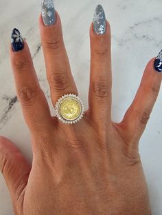 a woman's hand with blue and white nail polish holding a gold coin ring