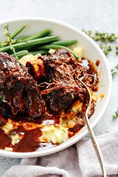 a bowl filled with meat and mashed potatoes covered in gravy next to green beans