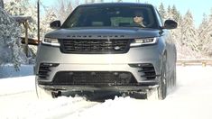 a silver range rover driving down a snow covered road with trees in the back ground