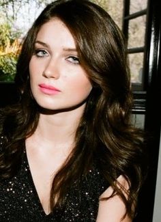 a woman with long brown hair wearing a black dress and posing for a photo in front of a window