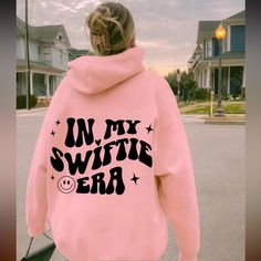 a woman wearing a pink hoodie with the words in my swiffie era printed on it