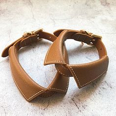 two brown leather dog collars sitting on top of a white floor next to each other