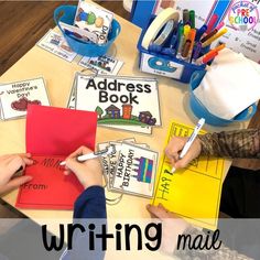 two children writing mail on a table with their teacher's hand and pencils