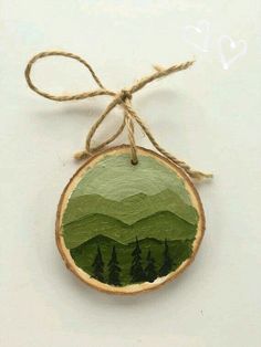 a wooden ornament with trees and mountains painted on the front, hanging from a string