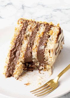 a piece of cake on a white plate with a gold fork next to the slice