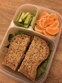 a plastic container filled with food on top of a wooden table next to sliced oranges and cucumbers