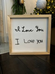 a sign that says i love you in black ink on a wooden frame next to a christmas tree