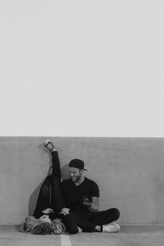 black and white photograph of two people sitting on the ground, one holding up a bottle