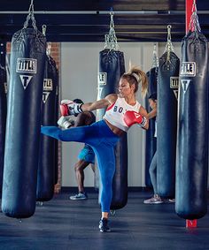 two women kick punches at each other in a boxing ring with punching gloves hanging from the ceiling