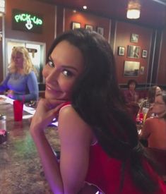 a woman in a red dress sitting at a bar with her hand on her chin