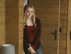 a woman standing in front of a wooden door with her hands on her hips and looking at the camera