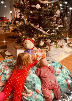 two children are laying in front of a christmas tree and looking at an open book