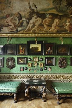 a room with green walls and paintings on the wall, two benches in front of them