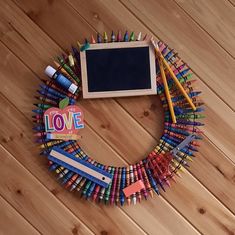 a wreath made out of crayons and pencils with a chalkboard in the middle