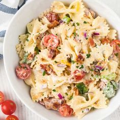 a white bowl filled with pasta salad next to tomatoes and broccoli on a blue and white towel