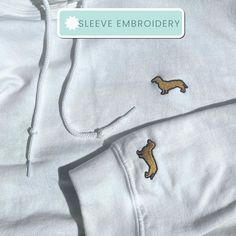 "Everyone needs a comfy basic hoodie to curl up in, so go for one that's soft, smooth, and stylish. This one has a little extra touch, embroidered in Gold with our signature smooth hair dachshund on the chest as well as on both sleeves. Please check out our other listings as well for variations of this hoodie, including  a wire hair dachshund! 👕 Product Details * 50% pre-shrunk cotton, 50% polyester * Embroidered in Birmingham, UK for sizes up to 2XL for UK customers; 2XL+ embroidered and shipp Winter Hoodie With Embroidered Patch Long Sleeve, Hoodie Sleeve Embroidery, Winter Long Sleeve Hoodie With Embroidered Patch, Trendy Embroidered Hooded Sweatshirt, White Hooded Hoodie With Embroidered Patch, Oversized Embroidered Cotton Hoodie, Dog Embroidery Sweatshirt, Black Embroidered Long Sleeve Hoodie, Embroidered Dachshund