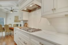 a kitchen with white cabinets and marble counter tops is pictured in this image, there are chairs around the stove