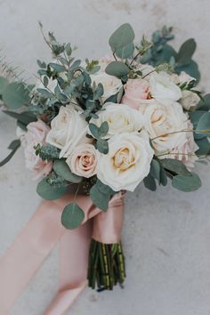 a bridal bouquet with white roses and greenery on the bottom, along with dusty pink ribbon