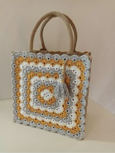 a crocheted bag is sitting on a white table with a brown handle and handles