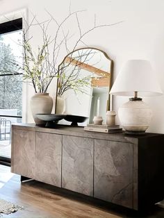 a living room with a large mirror and vases on top of the sideboard