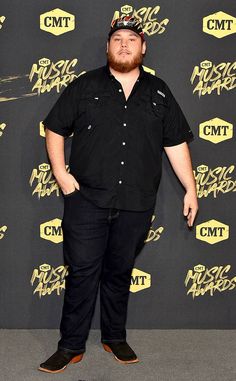 a man in black shirt and hat standing on the red carpet at an awards event