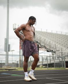 a shirtless man standing on a tennis court with his hands behind his back as he looks down