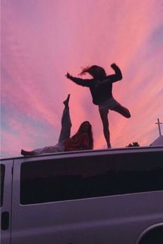 two people are standing on the roof of a van with their arms in the air