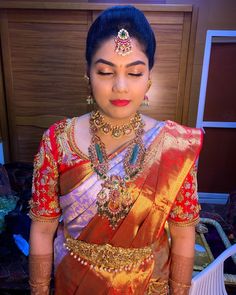 a woman in a red and gold sari with jewelry on her head, looking down