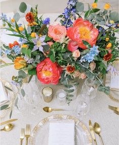 an arrangement of flowers and greenery on a table set for a formal dinner or reception