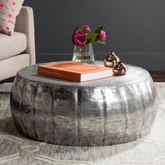 a coffee table with a book and flowers on it in front of a gray couch