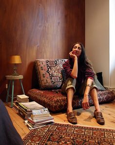 a woman sitting on top of a couch in a living room next to a pile of books