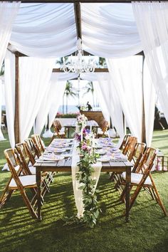 a table set up for an outdoor wedding with white draping and floral centerpieces