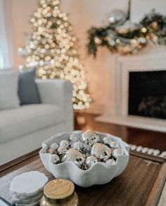 a christmas tree is in the background behind a bowl of ornaments on a coffee table