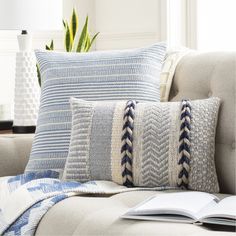 a couch with two pillows and a book on top of it next to a plant